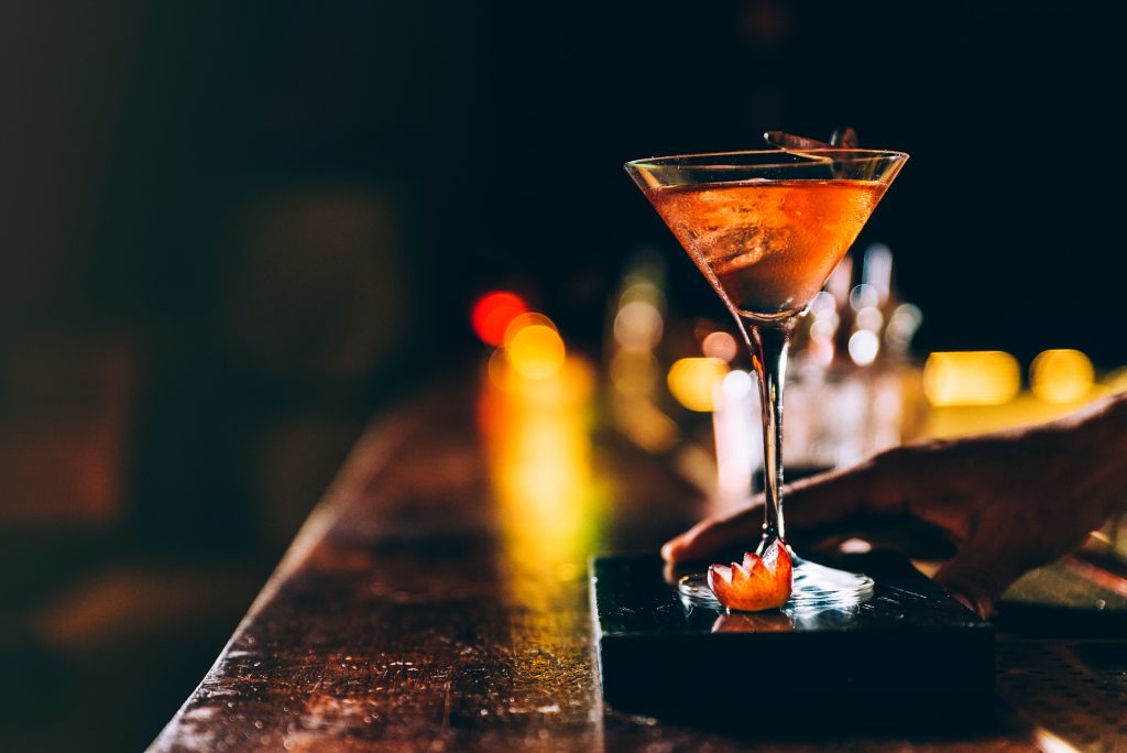 Elegant cocktail served in a martini glass, garnished with sliced fruit, on a bar counter at night.
