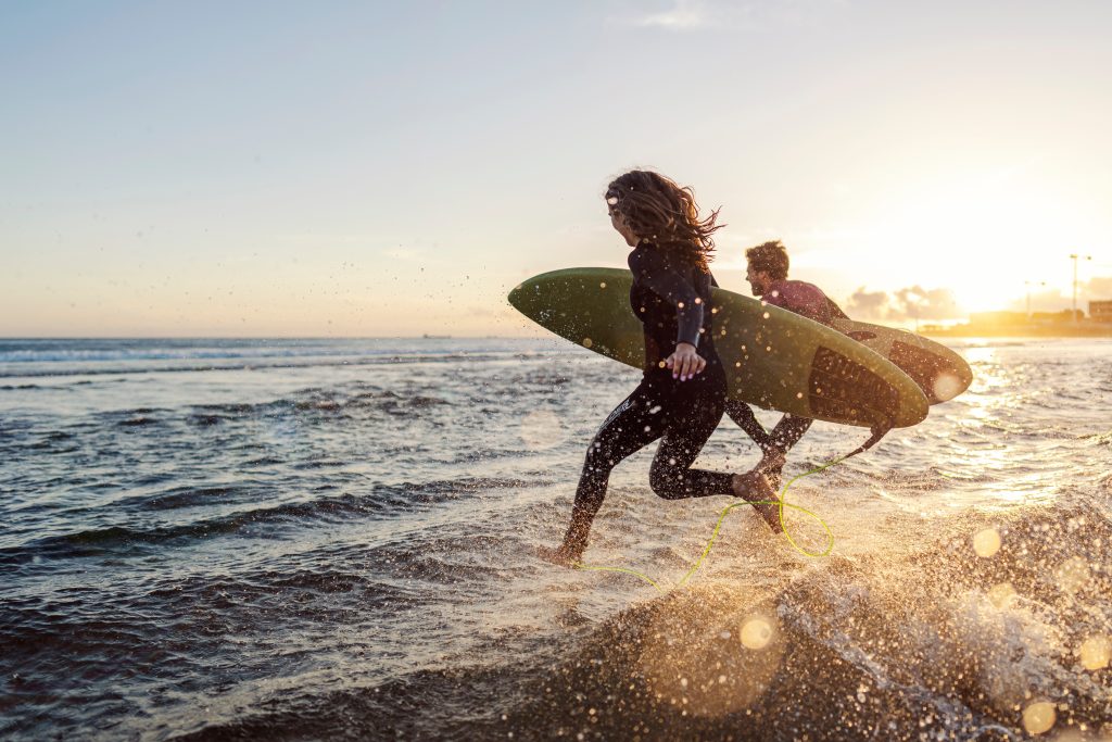Two surfers run into the ocean with boards at sunset, splashing through shallow waves.