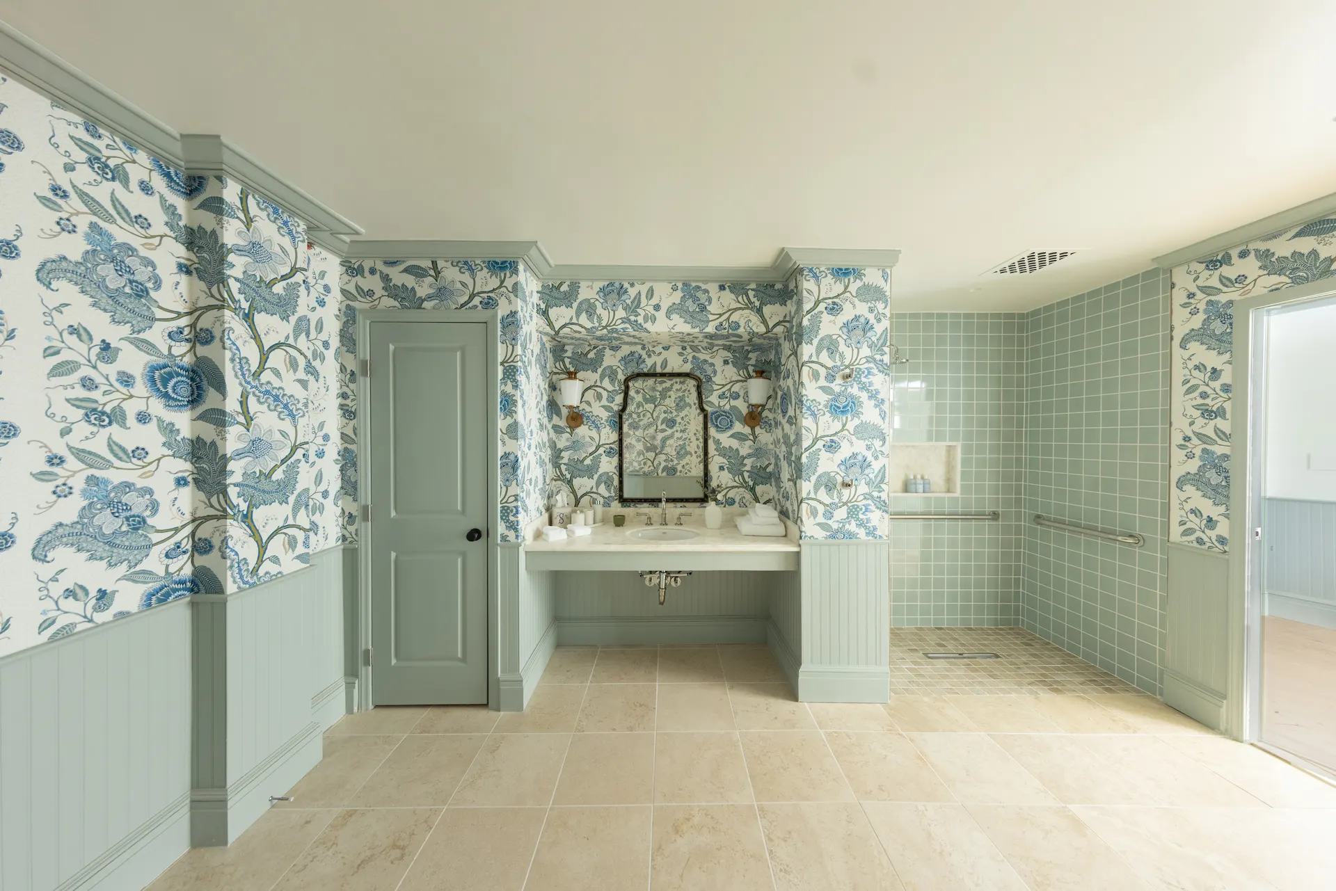 Bathroom with floral wallpaper, green wainscoting, marble double sink, and walk-in shower with green tiles.