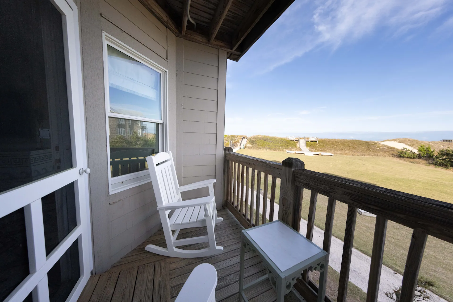 Small porch with white rocking chair, glass-top table, and views of grassy path leading toward the beach.
