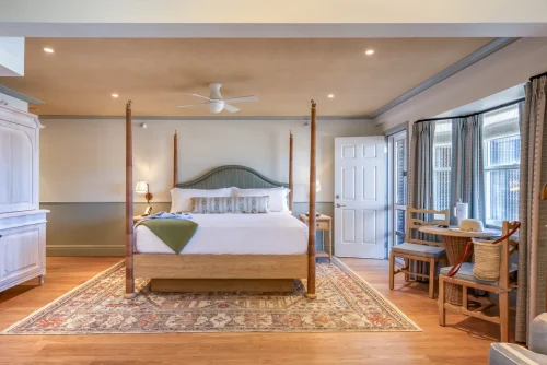 Spacious bedroom with canopy bed, patterned rug, wooden furniture, and cozy sitting area near windows.