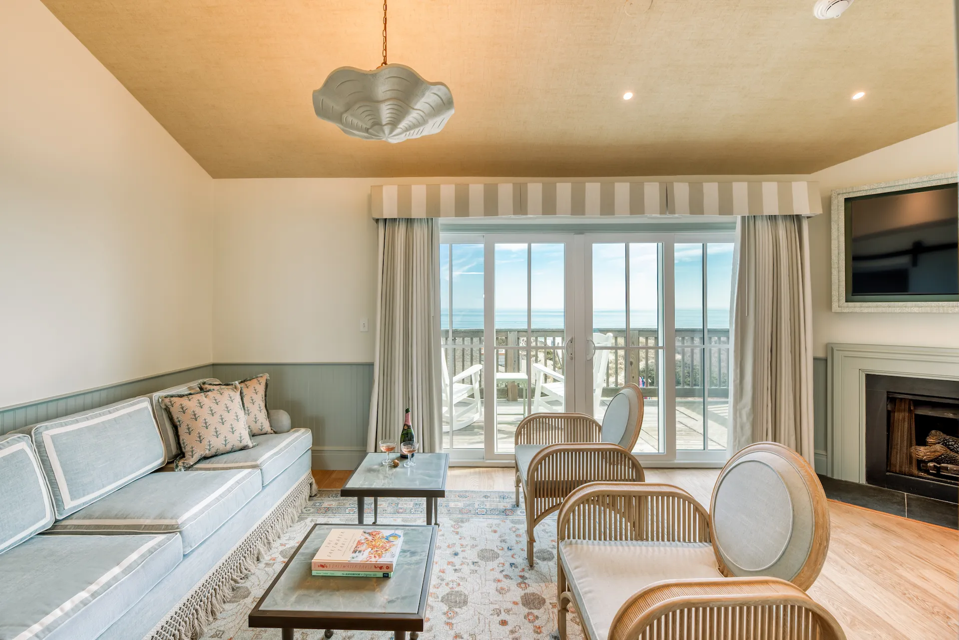 Coastal living room with pastel seating, sliding glass doors, ocean view, and elegant lighting.