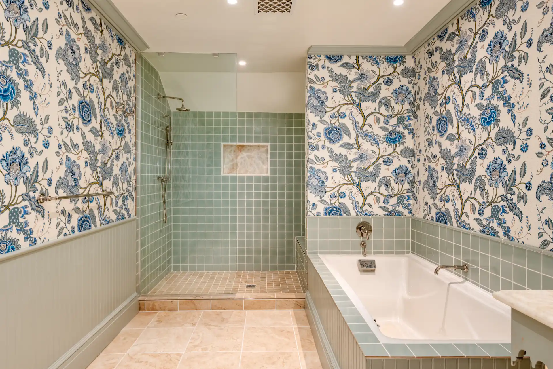 Bathroom with glass shower, green tiles, soaking bathtub, and floral-patterned wallpaper in blue and white.