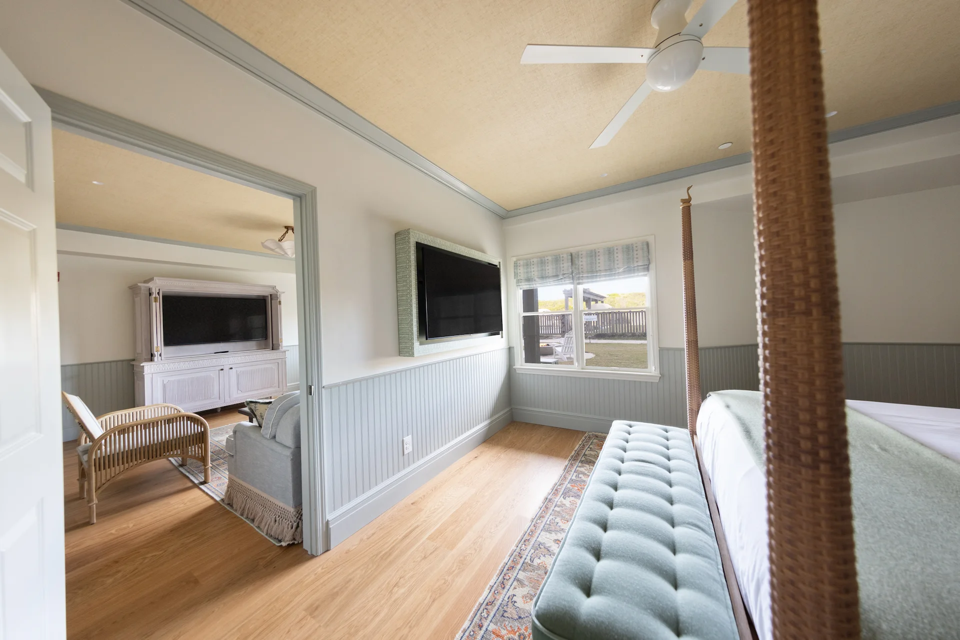 Bright coastal-style bedroom with mint accents, flat-screen TV, and view into adjoining sitting area.