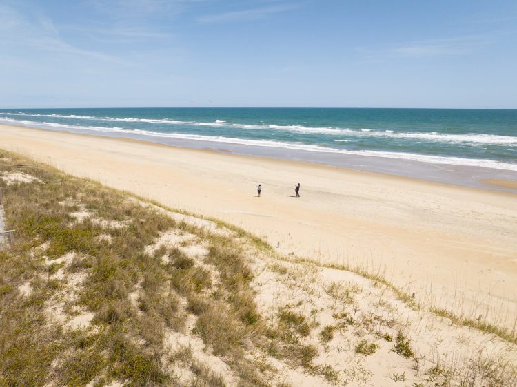 Aerial view of a wide sandy beach with ocean waves and dunes