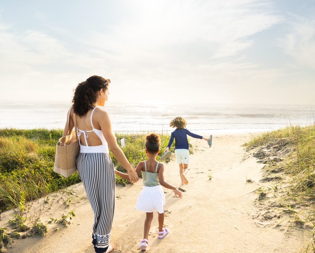 Family walking along a sandy beach path toward the ocean