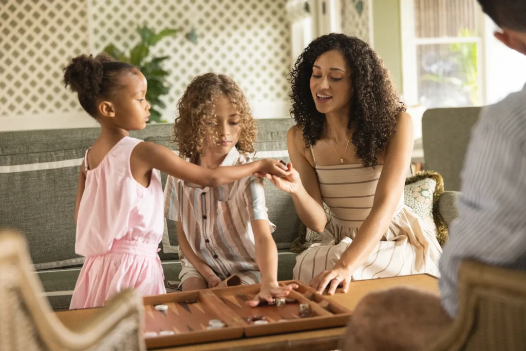 Family enjoys playing a board game together in a cozy, sunlit living room setting.