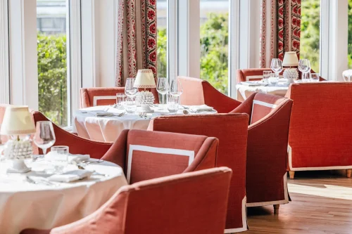 Elegant dining room at Theodosia with white tablecloths, red chairs, and soft natural light from large windows.