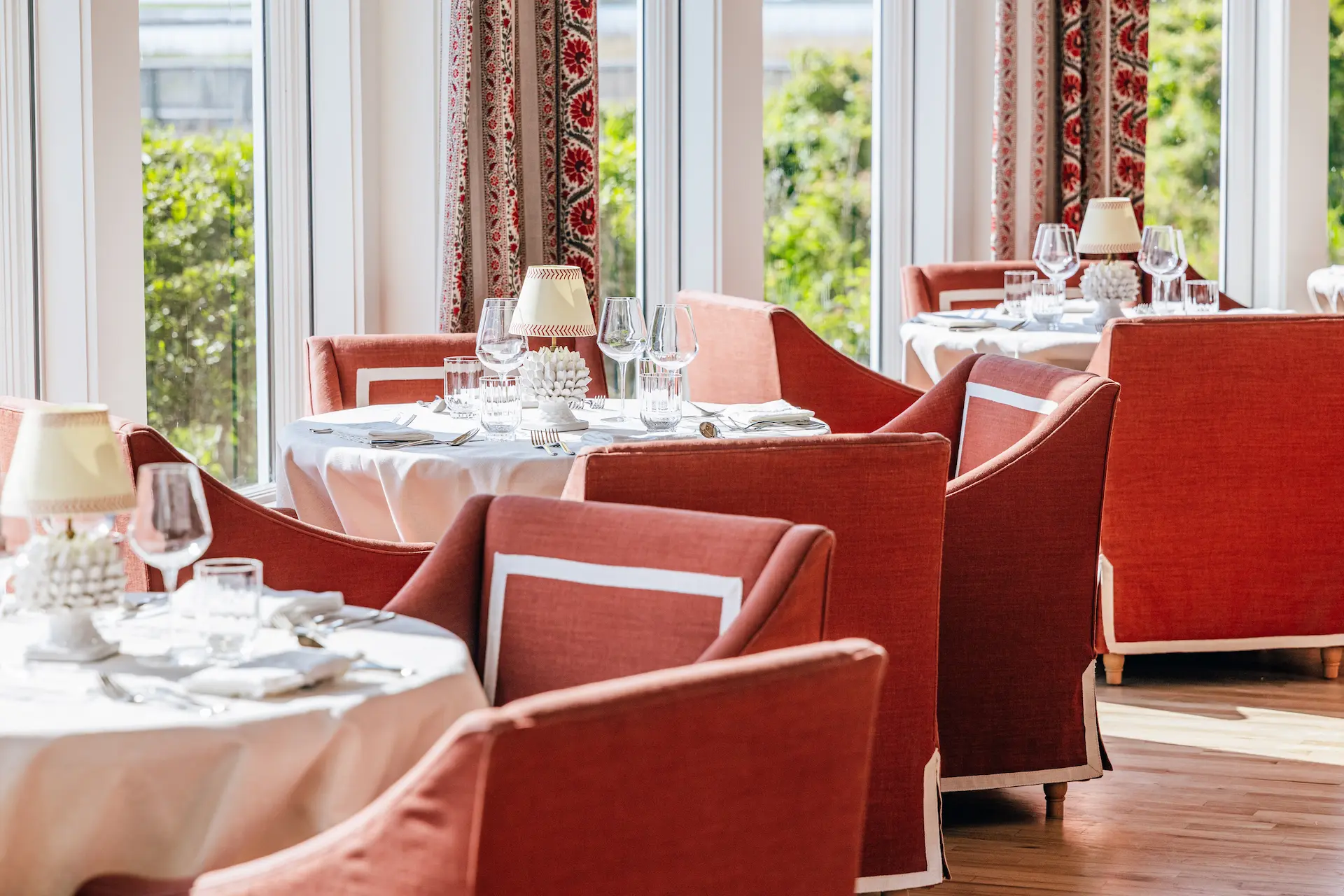 Elegant dining room at Theodosia with white tablecloths, red chairs, and soft natural light from large windows.