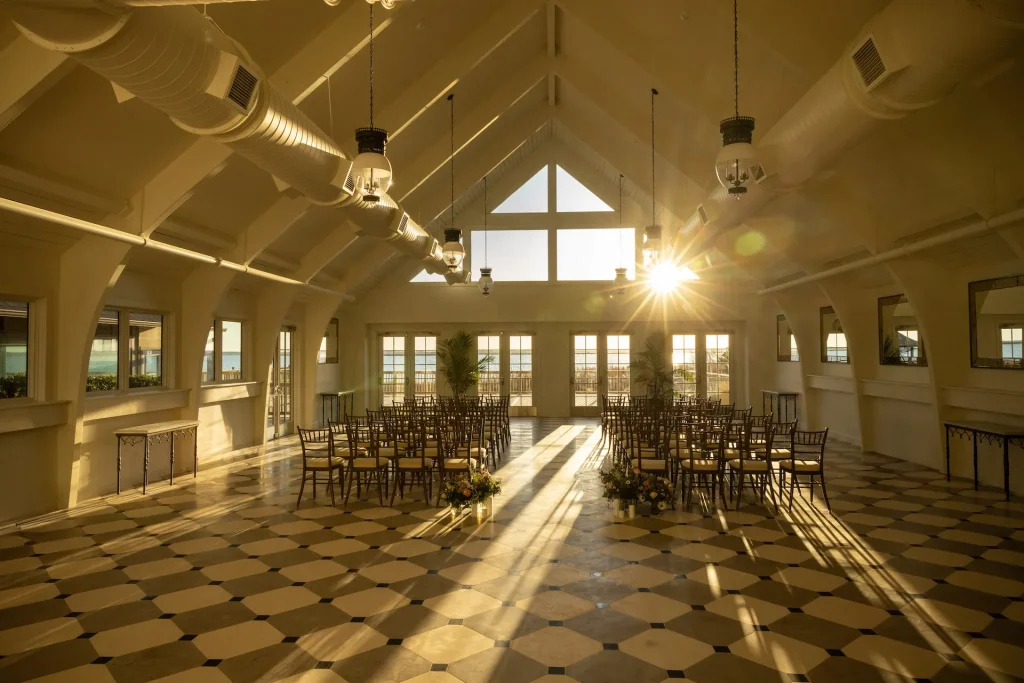 Elegant waterfront venue with vaulted ceilings, checkered tile floors, and round tables set for a sunlit celebration.