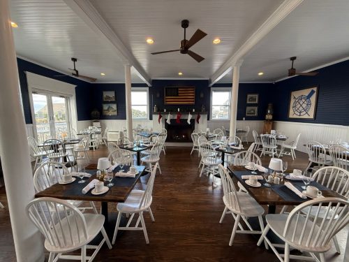 Festive nautical dining room with fireplace, stockings, and coastal views through large windows.