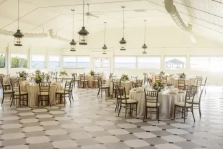 Spacious sunlit banquet hall with round tables elegantly set for an event overlooking water.