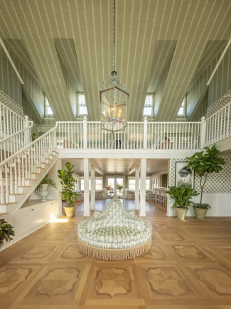 Grand foyer with patterned ceiling, central round bench, wooden floor, hanging chandelier, and potted indoor plants.