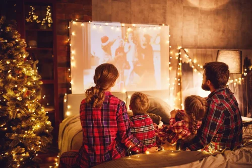 Family in matching pajamas watching a holiday movie by the Christmas tree, cozy night at The Sanderling Resort.