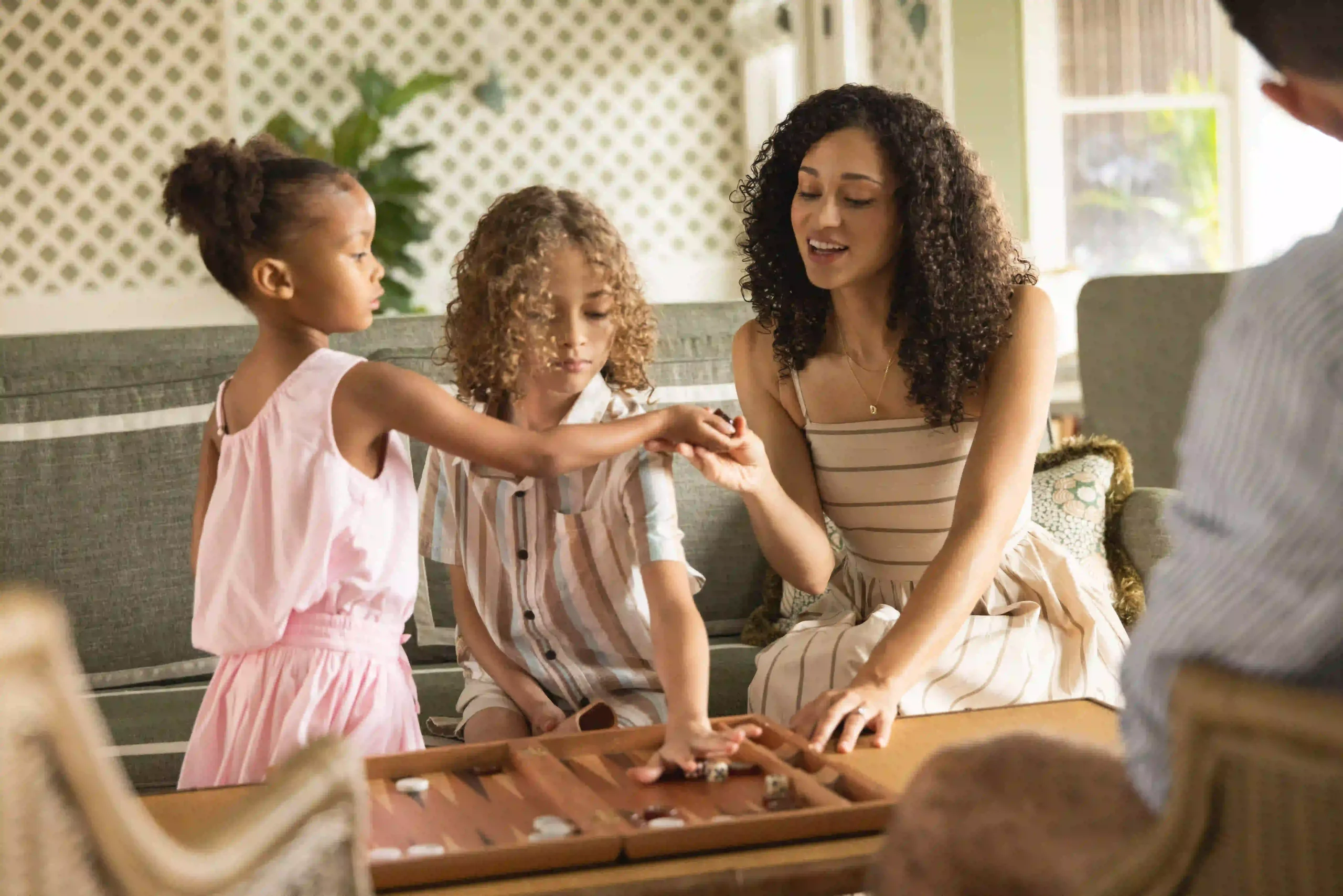 Family enjoys playing a board game together in a cozy, sunlit living room setting.