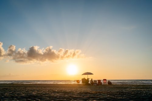 Beach umbrella and chairs looking at sunrise over ocean.